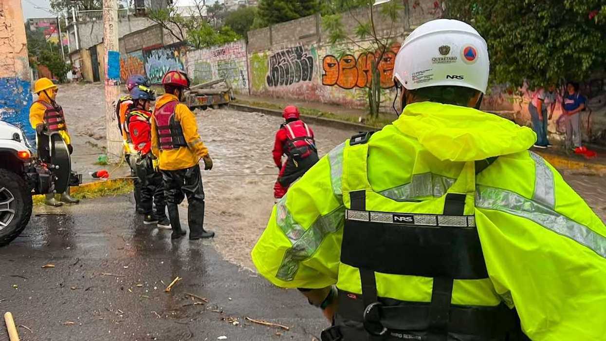 Personal de Protección Civil retira basura de una rejilla pluvial en una vialidad encharcada de Querétaro tras la lluvia nocturna.