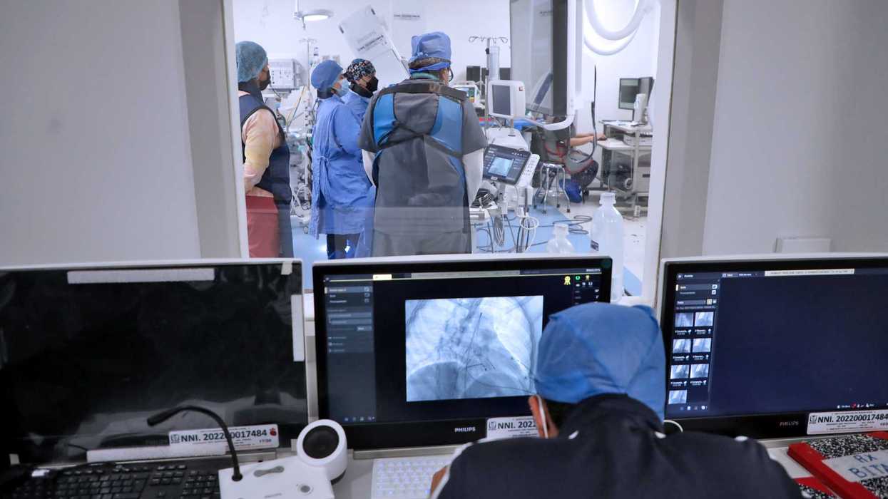 Personal médico con chalecos de protección en la sala de hemodinamia, visto desde la cabina de control con monitores