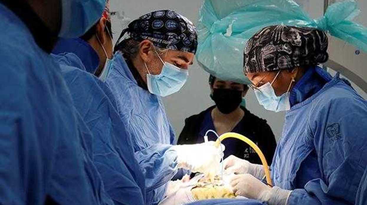 Personal médico realiza una cirugía en un quirófano, rodeando a un paciente bajo anestesia