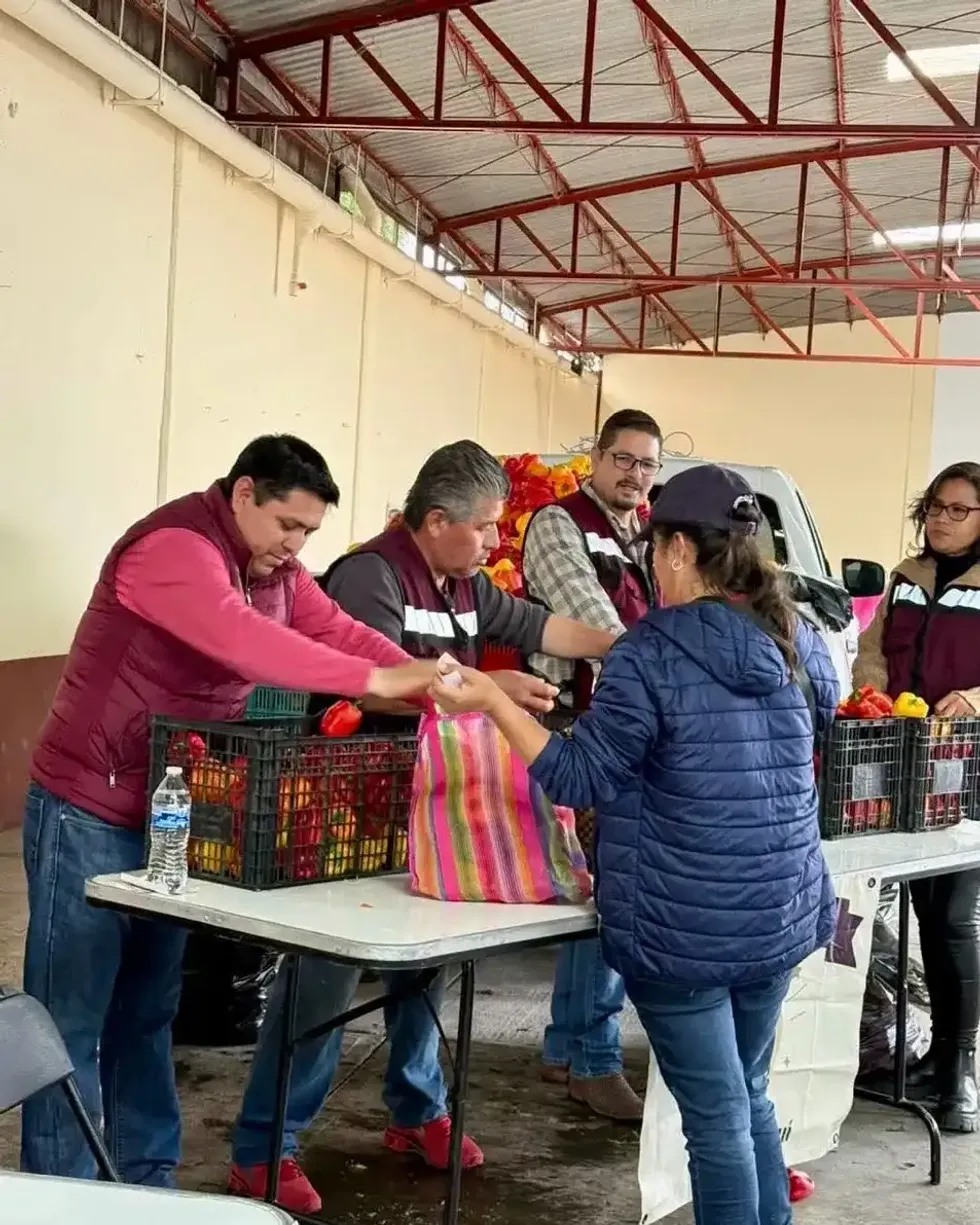 Personas con chalecos entregan verduras a una mujer sobre una mesa con cajas