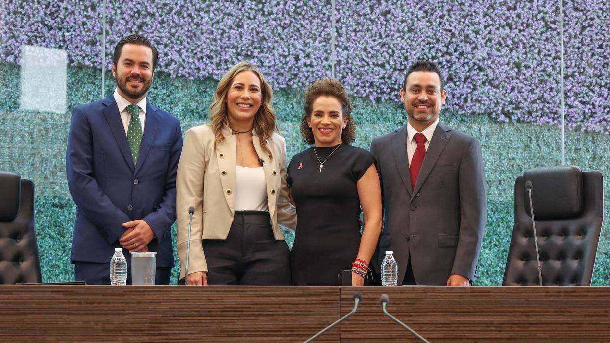 Personas de pie con la mano en el pecho en el recinto de la Legislatura de Querétaro, con una urna de cristal sobre una mesa en primer plano y público en la galería superior.