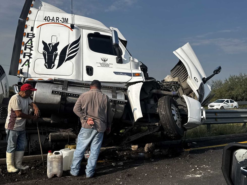 Personas observan el tractocami\u00f3n volcado mientras contin\u00faan las labores para retirar la unidad de la carretera Celaya\u2013Salamanca.