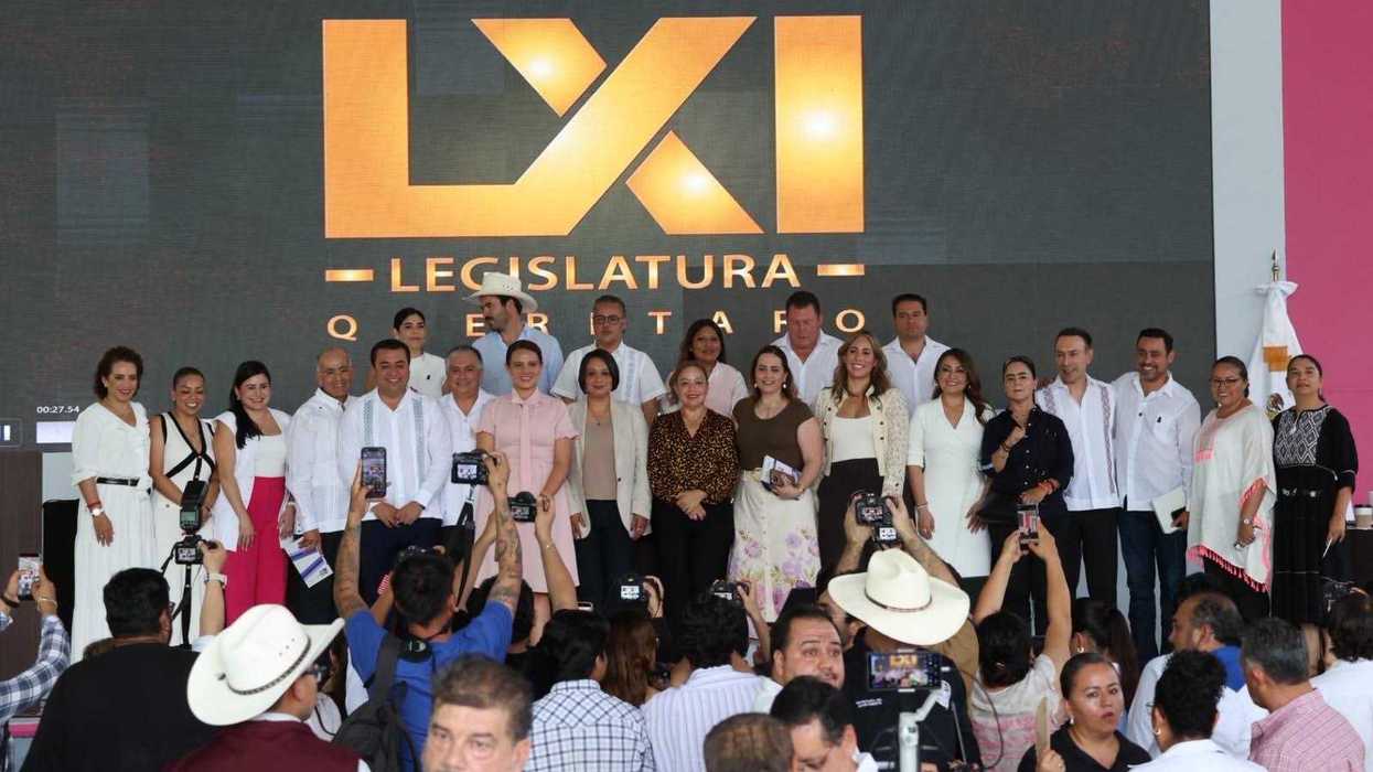 Personas posan en el escenario frente a una pantalla con el logotipo de la LXI Legislatura de Querétaro, con fotógrafos y público en primer plano.