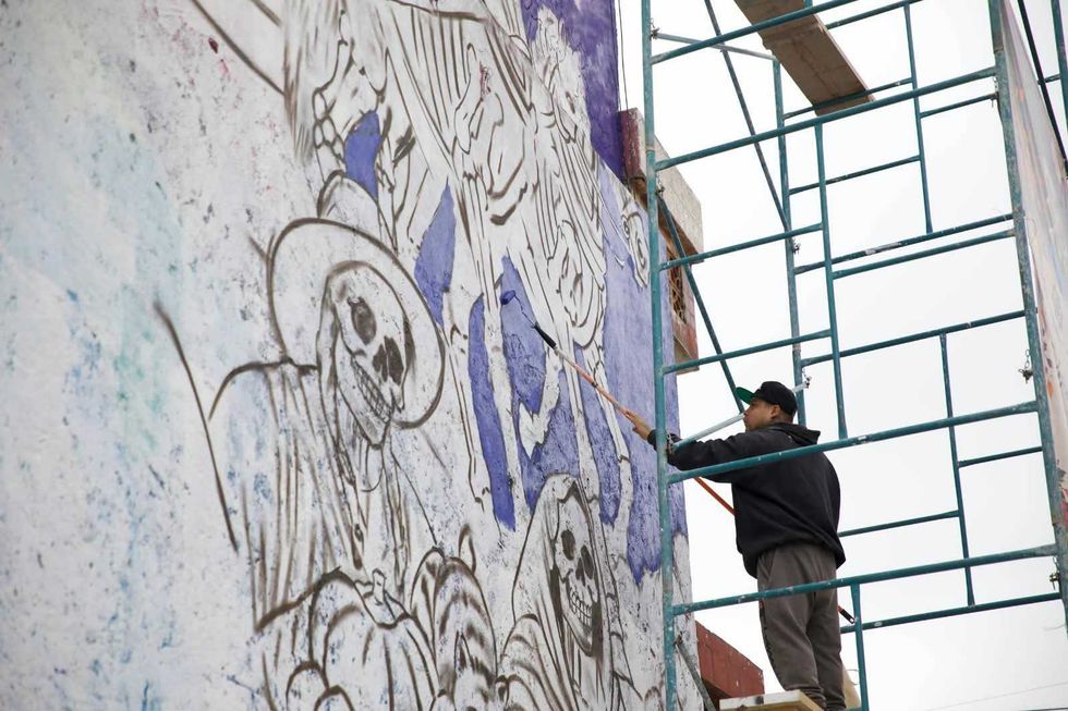Pintor con rodillo cubre de morado el boceto de una calavera con sombrero en el mural de D\u00eda de Muertos de San Juan del R\u00edo