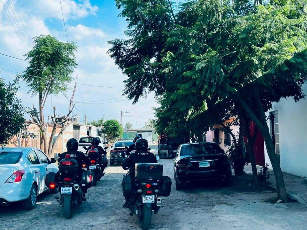 Polic\u00edas motorizados de San Juan del R\u00edo circulan en fila por una calle de terracer\u00eda entre veh\u00edculos particulares estacionados, durante un recorrido de vigilancia.