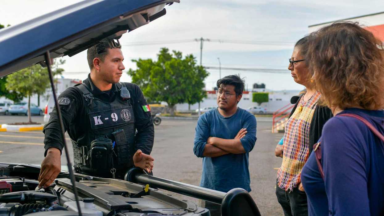 Policía de Corregidora conversa con ciudadanos junto a capó abierto durante taller de mecánica básica en Plaza Candiles, Querétaro.