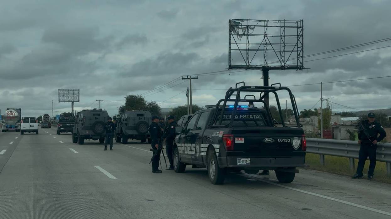 Policías estatales con armas largas vigilan dos vehículos blindados grises detenidos junto a patrullas sobre la autopista México-Querétaro, en San Juan del Río.