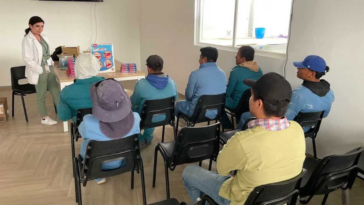 Profesional de salud presenta material sobre higiene bucal ante un grupo de asistentes sentados en un salón de Querétaro.