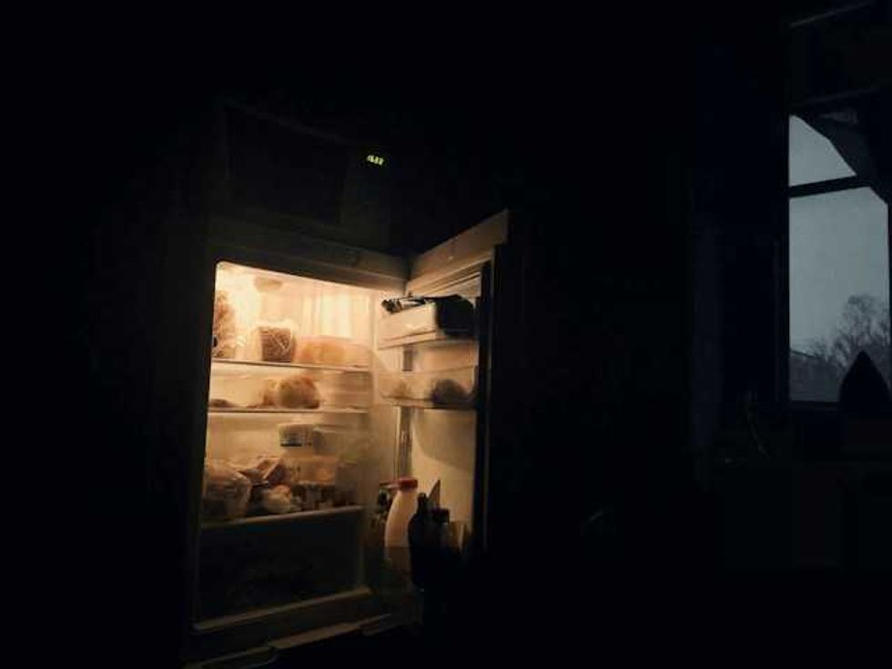 Refrigerador abierto en una cocina a oscuras, con alimentos iluminados en los estantes y botellas en la puerta