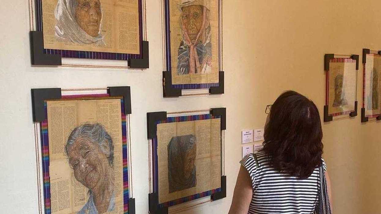 Retratos a lápiz de personas mayores en la exposición Una vida en la mirada, con una visitante observándolos en el MAQRO.