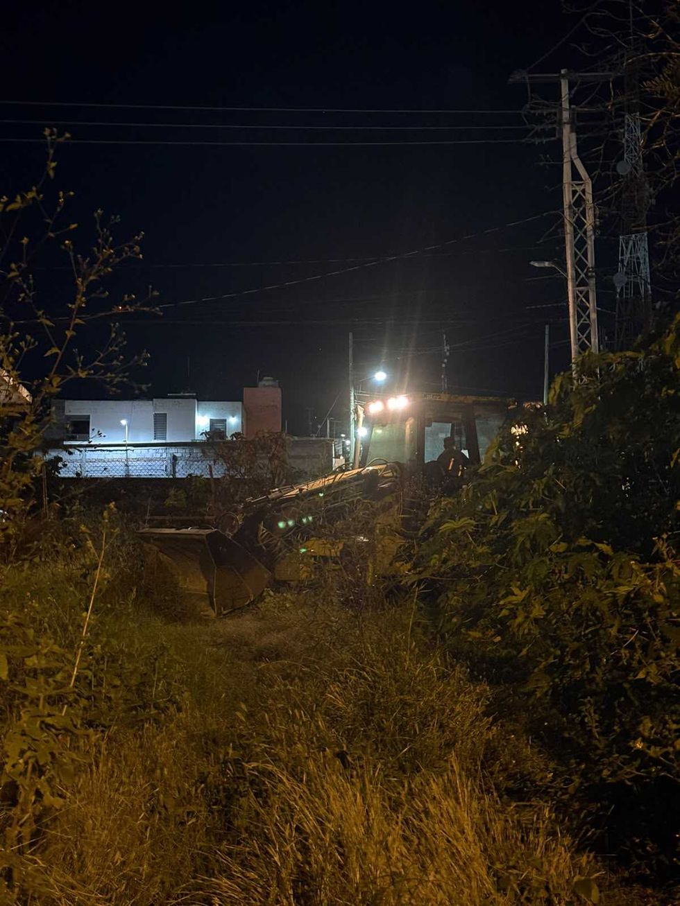 Retroexcavadora con luces encendidas avanza de noche entre la maleza del predio de avenida R\u00edo Moctezuma, en San Juan del R\u00edo
