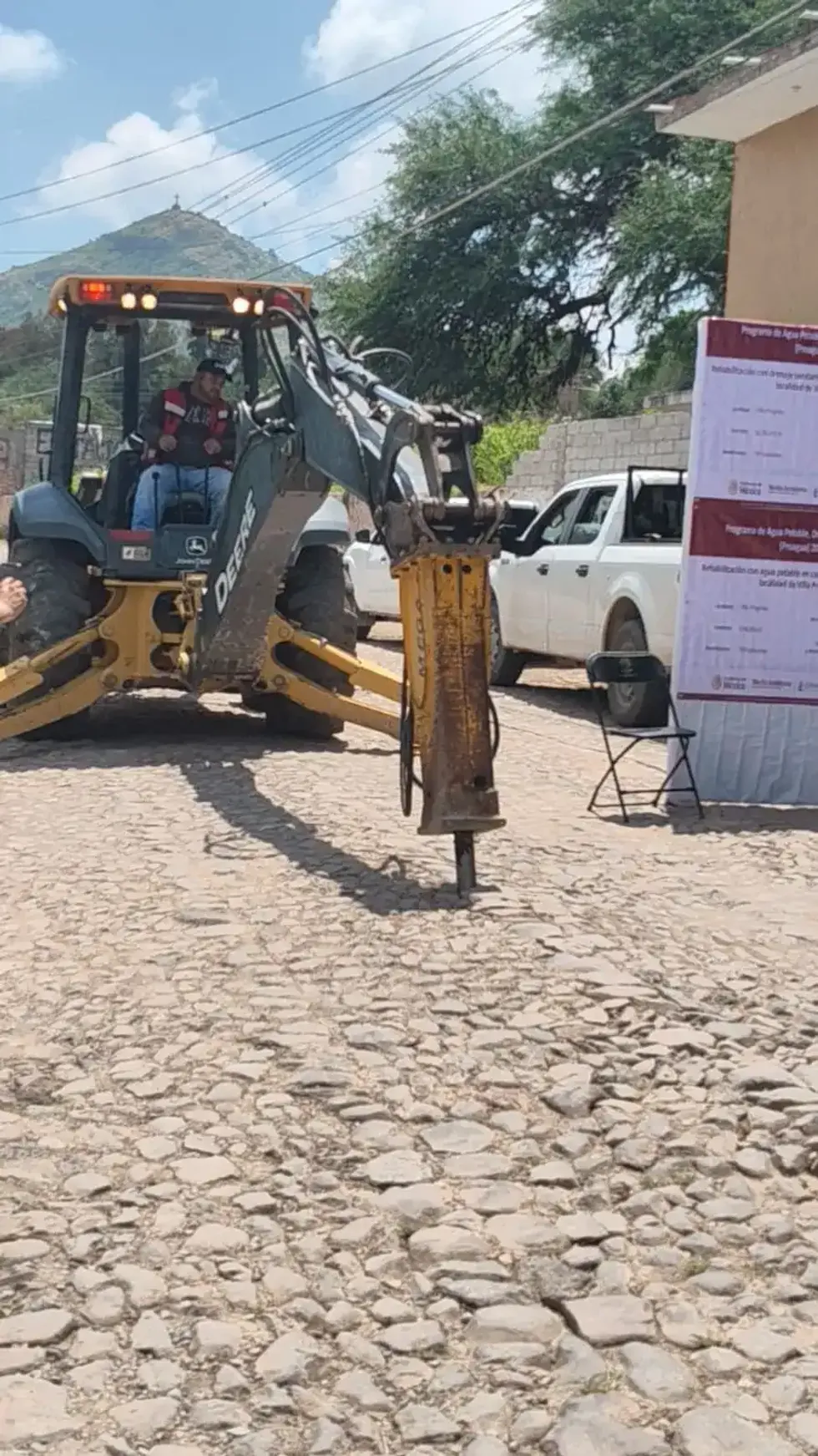 Retroexcavadora con martillo hidr\u00e1ulico en calle empedrada de Villa Progreso al inicio de la rehabilitaci\u00f3n del drenaje sanitario del Proagua 2026
