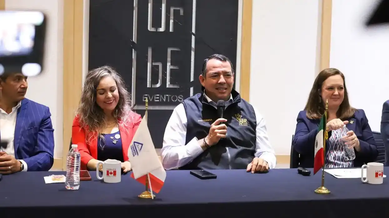 Roberto Cabrera Valencia habla por micrófono en la rueda de prensa; en la mesa aparecen las banderas de México y Canadá.