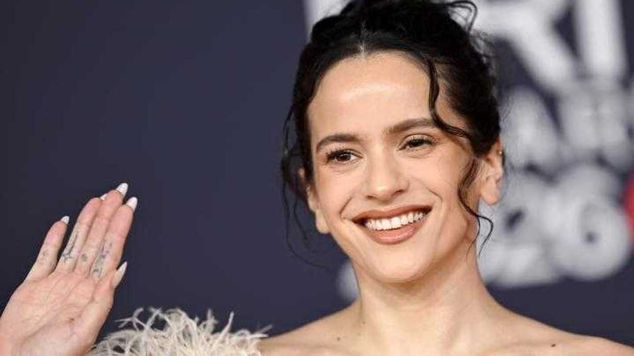 Rosalía, homenajeada con el Premio Billboard Salón de la Fama 2026, sonríe y levanta la mano para saludar, con el cabello recogido y un detalle de plumas blancas en el atuendo.