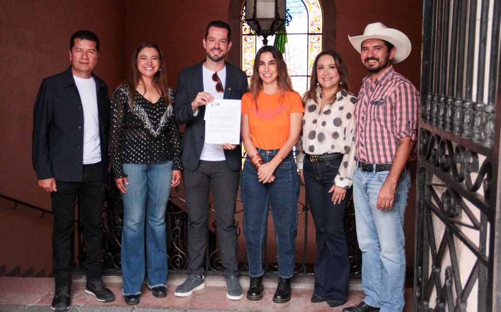 Seis personas posan en una escalera con barandal de herrer\u00eda mientras un hombre sostiene el documento con la solicitud de inspecci\u00f3n laboral para trabajadores del Tren M\u00e9xico-Quer\u00e9taro.