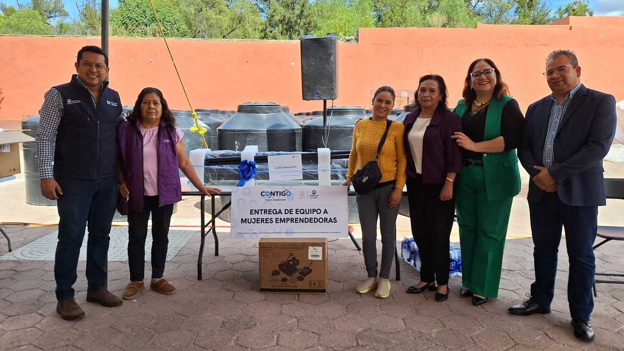 Seis personas posan junto a una manta con el texto "Entrega de equipo a mujeres emprendedoras", con cajas de equipo y tinacos al fondo, durante la entrega de equipamiento en Colón.