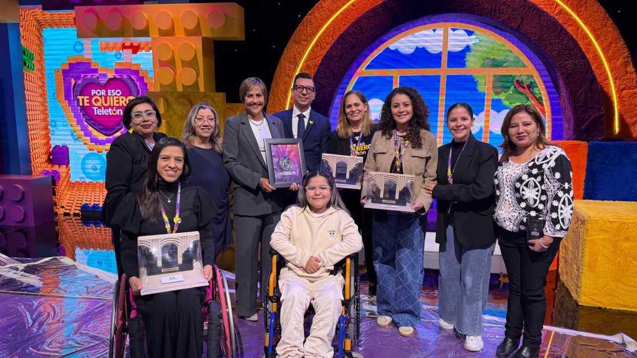 Seis personas posan sobre el escenario de un foro; un hombre sostiene la medalla Rincón Gallardo-Teletón enmarcada.