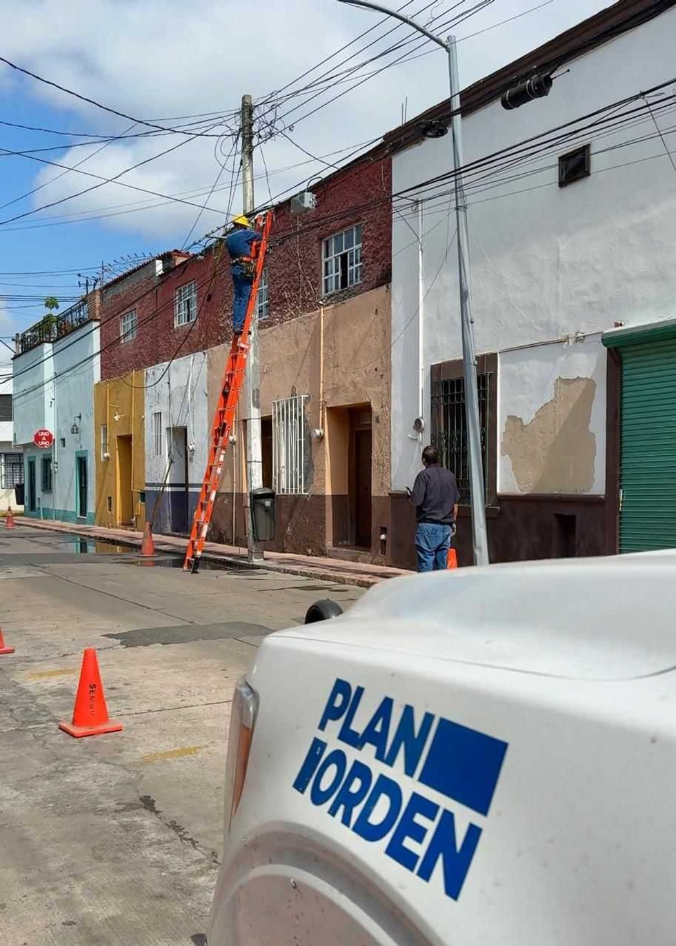 T\u00e9cnico en poste retira cableado en vialidad secundaria con veh\u00edculo de Plan Orden visible en primer plano
