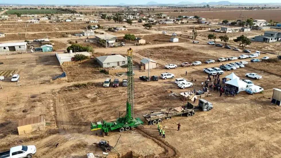 Torre de perforaci\u00f3n verde trabaja en un llano rural mientras se observan veh\u00edculos y personas reunidas