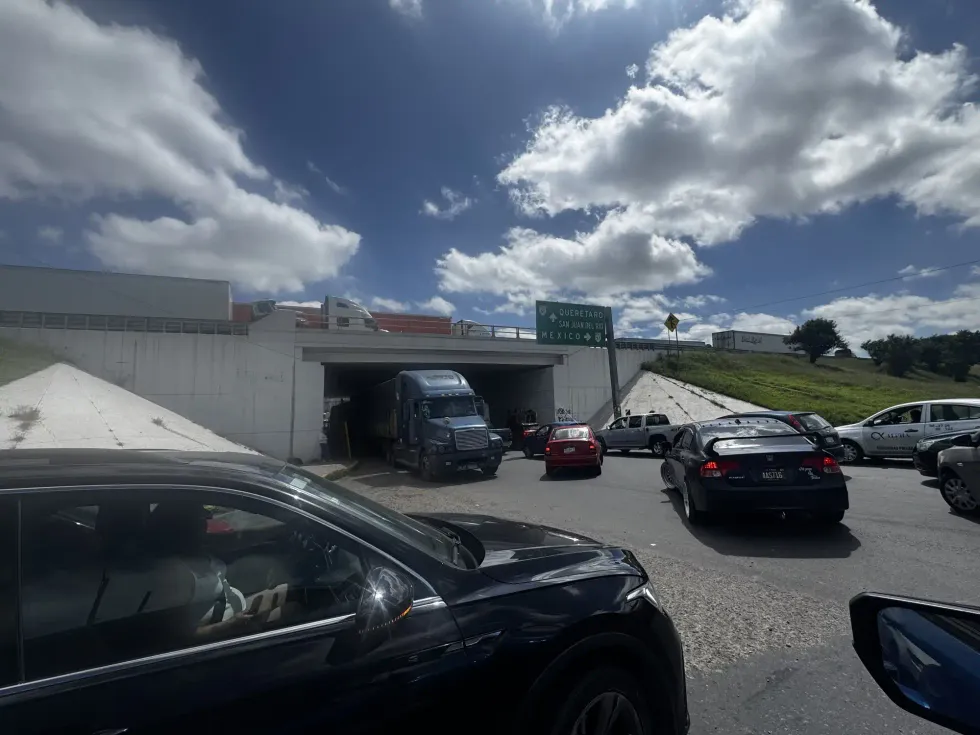 Tr\u00e1fico detenido frente al paso inferior de la autopista M\u00e9xico-Quer\u00e9taro en San Juan del R\u00edo, con se\u00f1al\u00e9tica de acceso a Quer\u00e9taro y M\u00e9xico visible al fondo