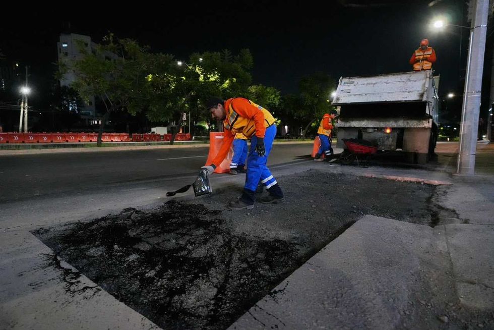 Trabajador con chaleco amarillo estrecha la mano de un hombre junto a un bache rellenado con asfalto en Quer\u00e9taro