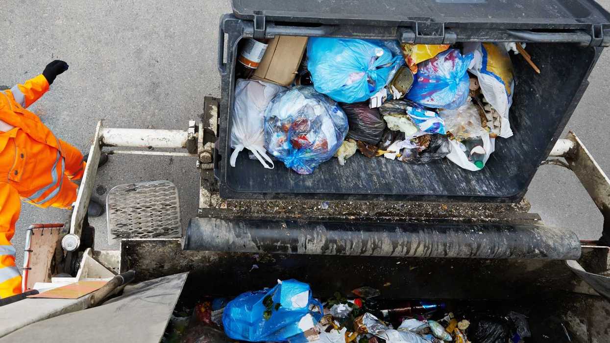 Trabajador con uniforme naranja vacía un contenedor en un camión de recolección de basura
