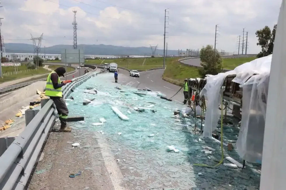 Trabajadores con chalecos de alta visibilidad retiran cristales de la calzada del distribuidor vial tras la volcadura del tractocami\u00f3n en Santa Rosa J\u00e1uregui, Quer\u00e9taro