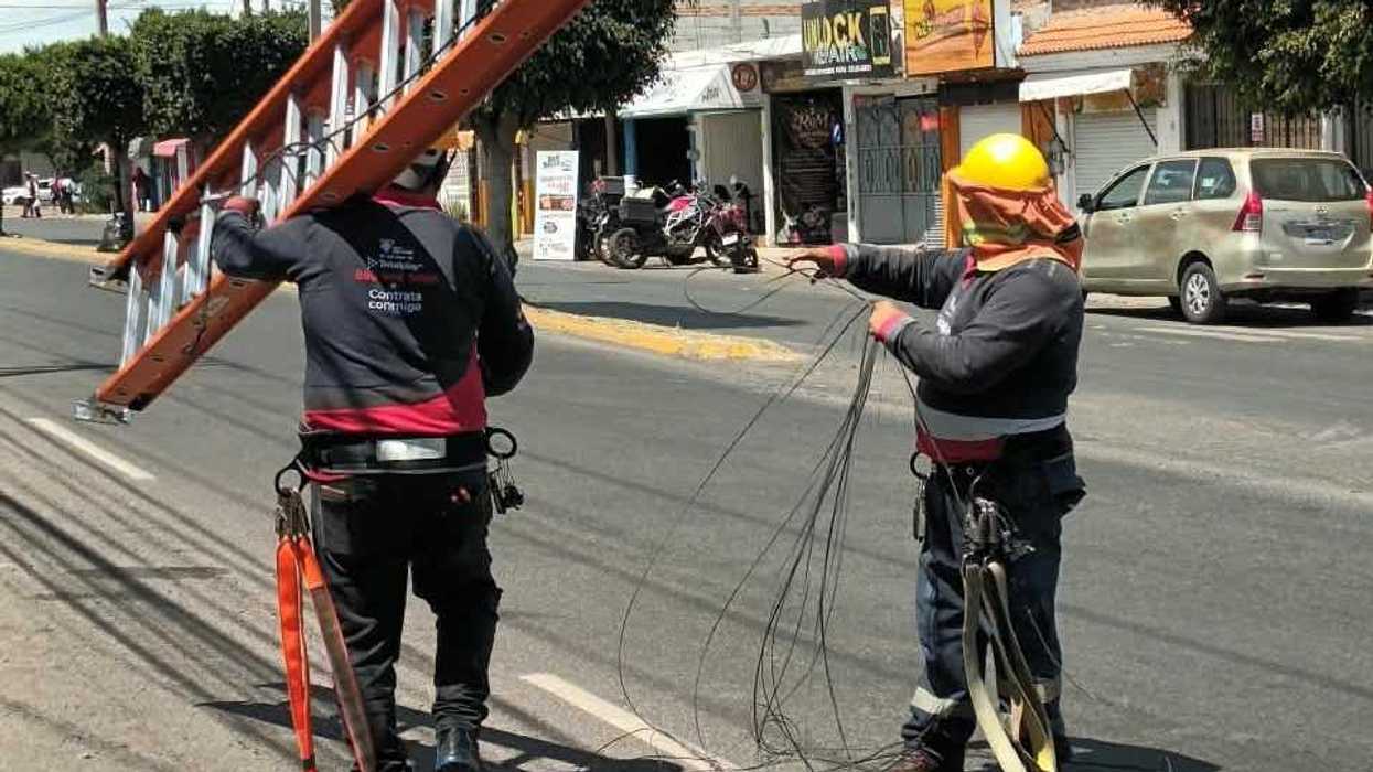 Trabajadores retiran cableado obsoleto en avenida Pedregoso de San Juan del Río; uno carga una escalera y otro jala cables