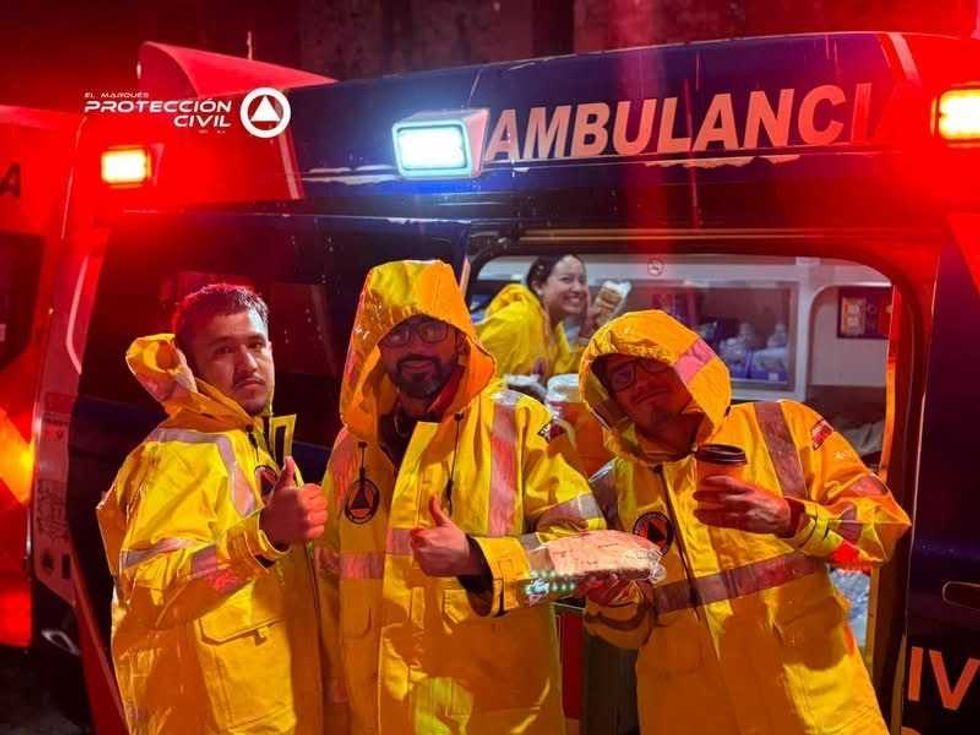 Tres elementos de Protecci\u00f3n Civil de El Marqu\u00e9s con trajes amarillos impermeables frente a una ambulancia durante la lluvia