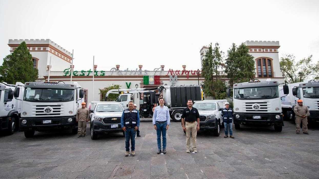 Tres hombres posan al frente de camiones y camionetas estacionados ante la fachada del Centro Municipal de El Marqués.