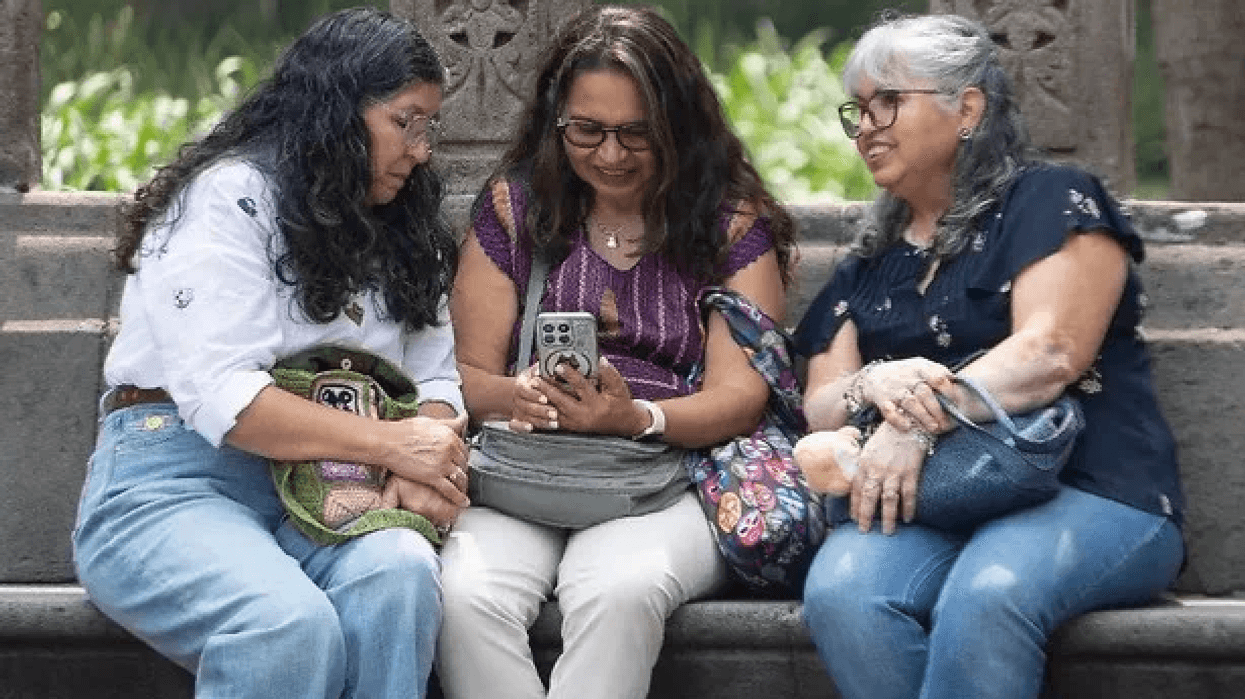 Tres mujeres sentadas en una banca de piedra miran un teléfono celular, imagen que ilustra el estudio de Nature sobre el dolor en mujeres.