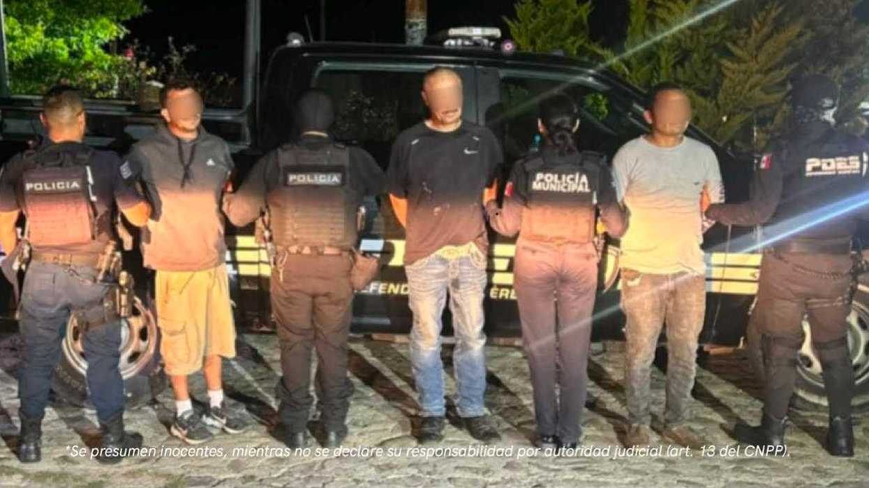 Tres personas con el rostro difuminado son custodiadas de espaldas por elementos de policía municipal y estatal frente a una patrulla, de noche, en Huimilpan, Querétaro.