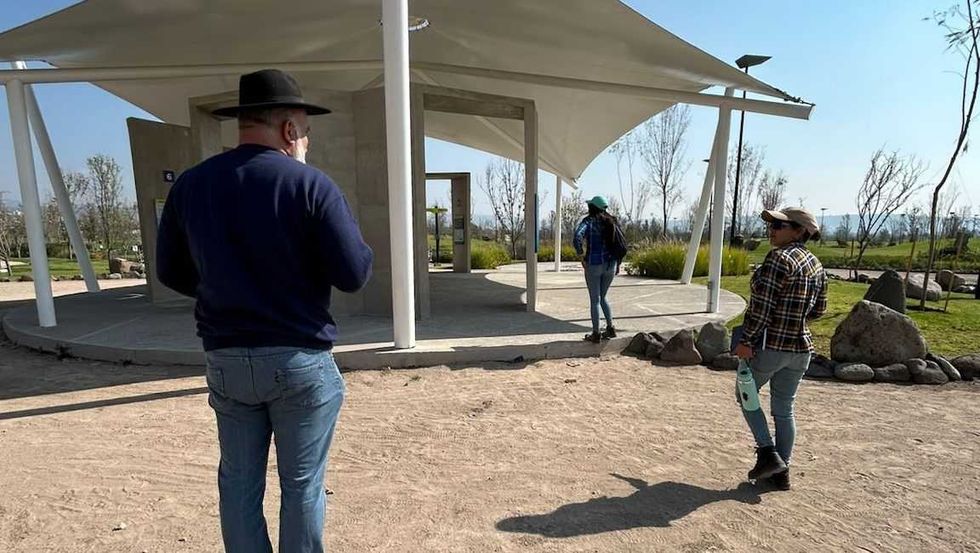 Tres personas recorren la explanada de un parque con estructura de membrana tensada y vegetaci\u00f3n