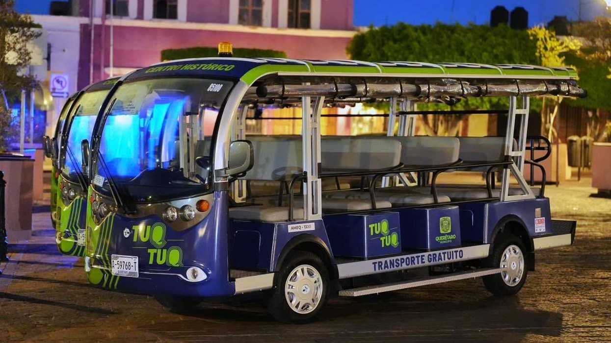 Tres unidades del transporte eléctrico gratuito estacionadas en el Centro Histórico de Querétaro, con una torre religiosa iluminada al fondo.