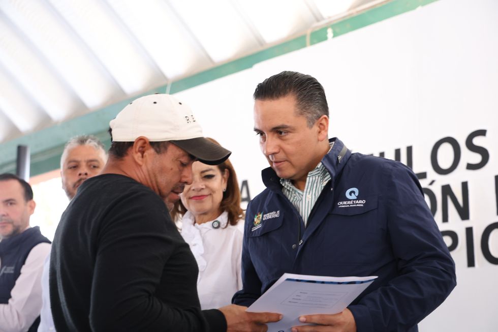 Un hombre con gorra y un funcionario con chamarra de la Secretar\u00eda de Gobierno sostienen un documento durante la entrega de t\u00edtulos de propiedad en Cadereyta de Montes.