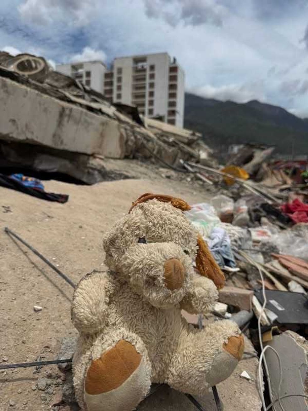 Un peluche queda entre los escombros de un edificio derrumbado, con un edificio da\u00f1ado al fondo.