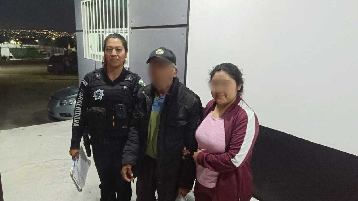 Un policía de la SSPM Corregidora camina junto a un hombre adulto mayor y una mujer, tomados del brazo, frente a un edificio institucional durante la noche.