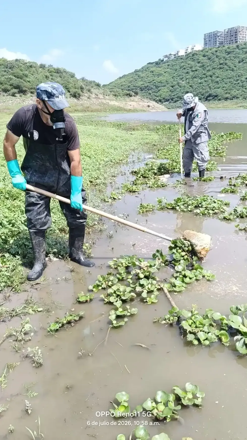Un trabajador con overol, guantes y mascarilla retira material del agua en la presa El Bat\u00e1n.