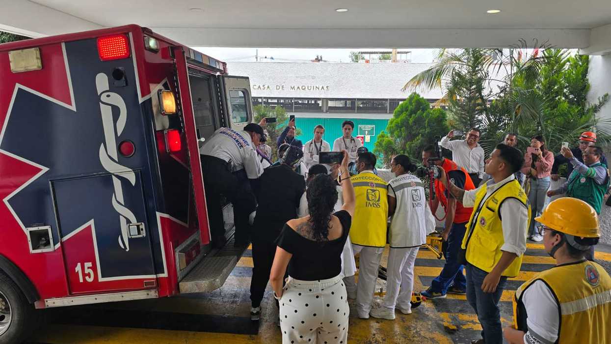 Una ambulancia con el número 15 frente al acceso a Urgencias, rodeada de personal médico y de Protección Civil.
