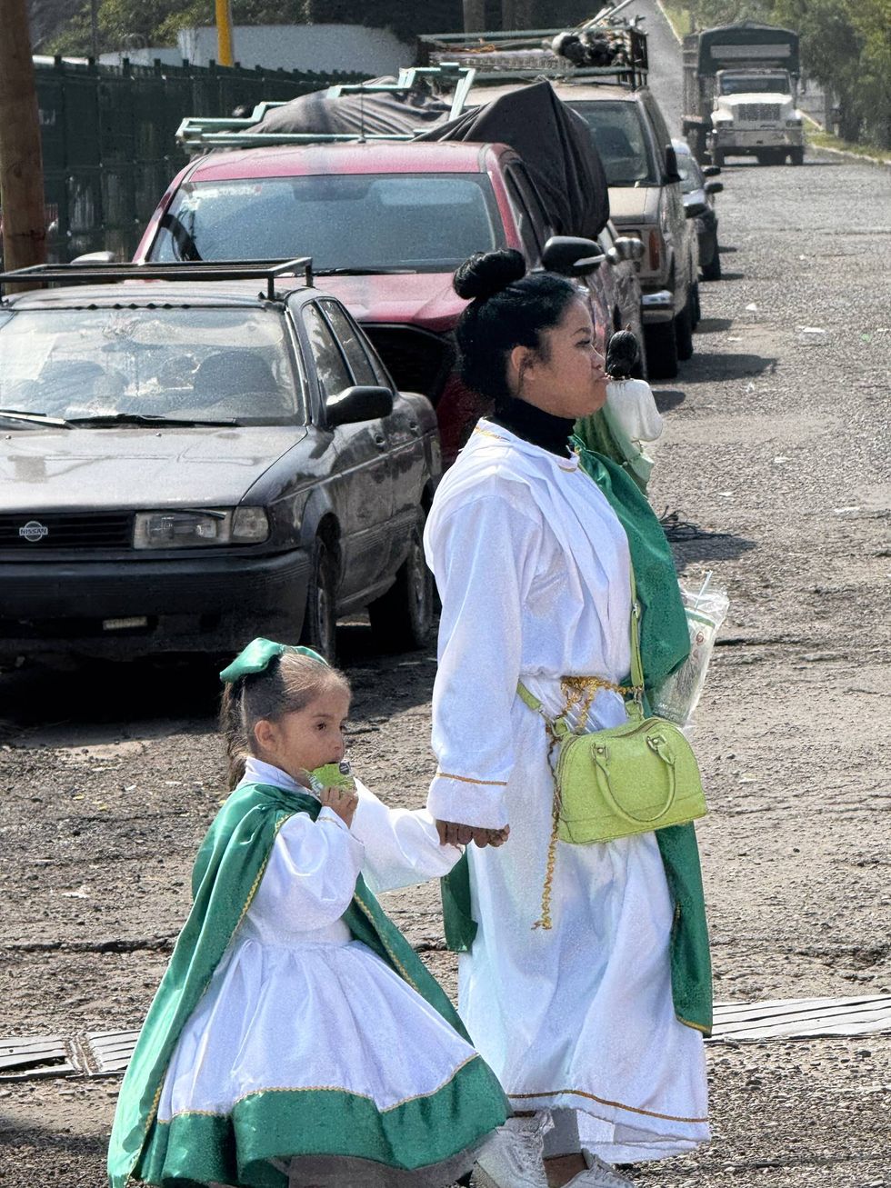 Una mujer y una ni\u00f1a con t\u00fanica blanca y capa verde caminan tomadas de la mano durante la peregrinaci\u00f3n a San Judas Tadeo en La Noria, El Marqu\u00e9s.