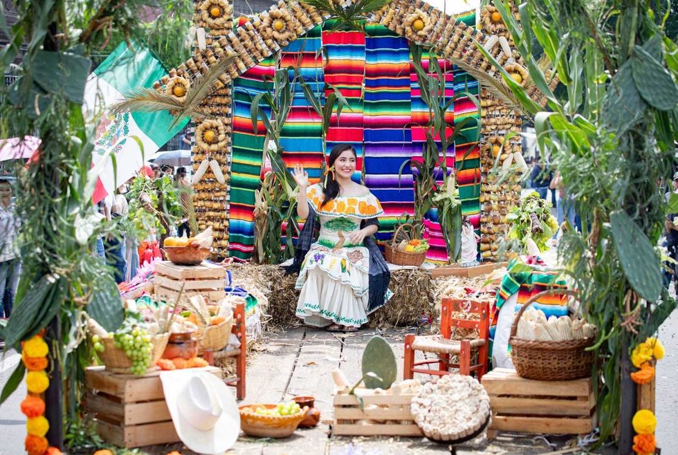 Una participante saluda desde un carro aleg\u00f3rico decorado con mazorcas, textiles y productos agr\u00edcolas.