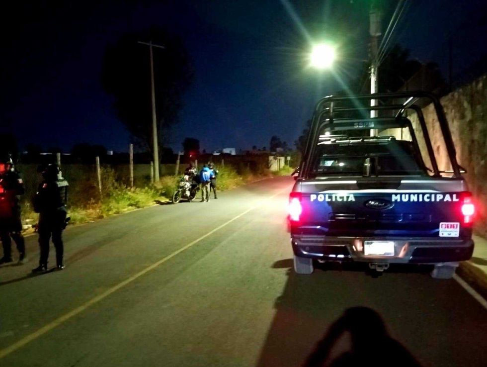 Una patrulla de la Polic\u00eda Municipal de San Juan del R\u00edo se detiene de noche junto a una motocicleta y dos personas en una vialidad, mientras otros elementos observan desde la banqueta.