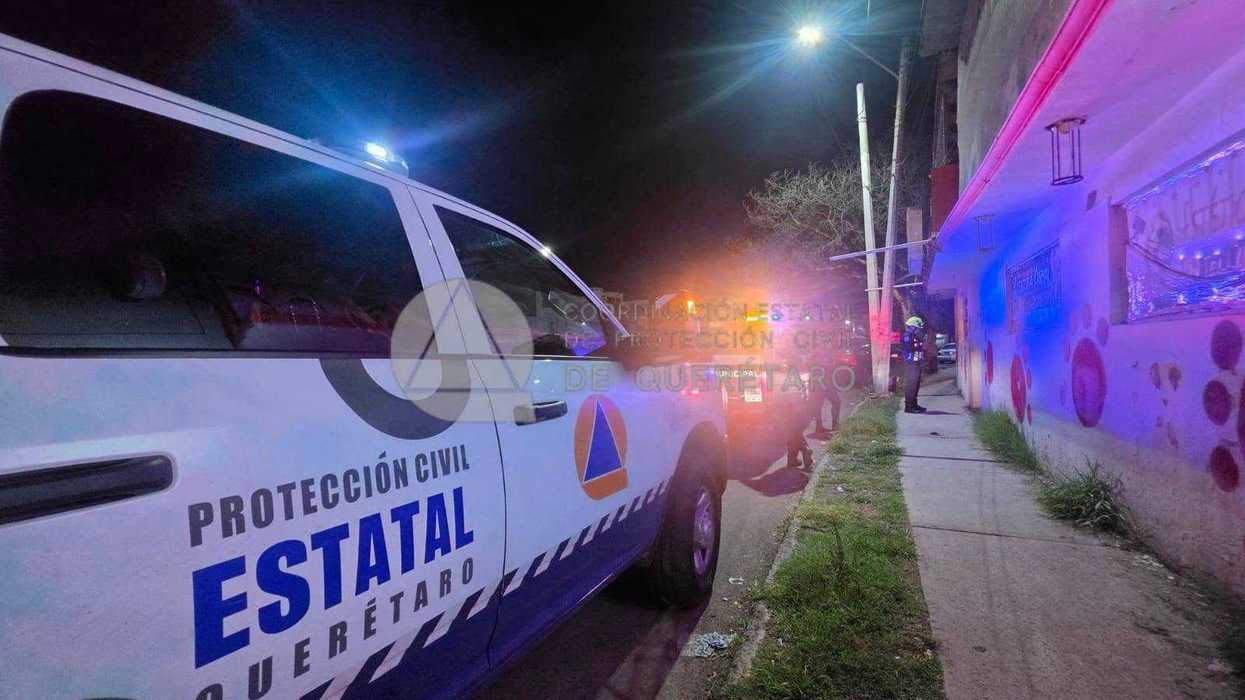 Unidad de la Coordinación Estatal de Protección Civil de Querétaro estacionada de noche frente a un comercio en la colonia El Vergel, con luces de emergencia encendidas y personal en la banqueta.