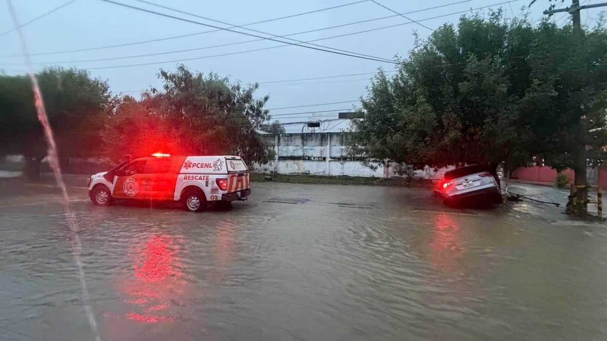 Unidad de rescate de Protección Civil de Nuevo León en una calle inundada, junto a un vehículo parcialmente hundido durante las lluvias.
