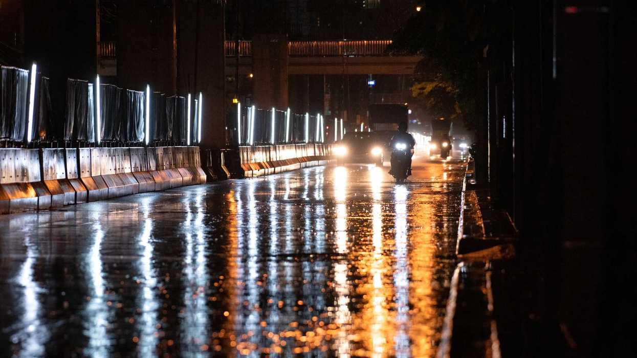 Vehículos circulan durante una noche lluviosa sobre una vialidad con el pavimento mojado.