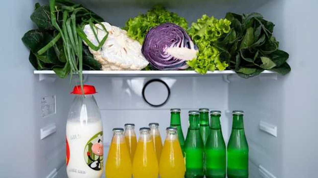Verduras de hoja, coliflor y col morada en un estante del refrigerador, con una botella de leche y refrescos embotellados en el nivel inferior