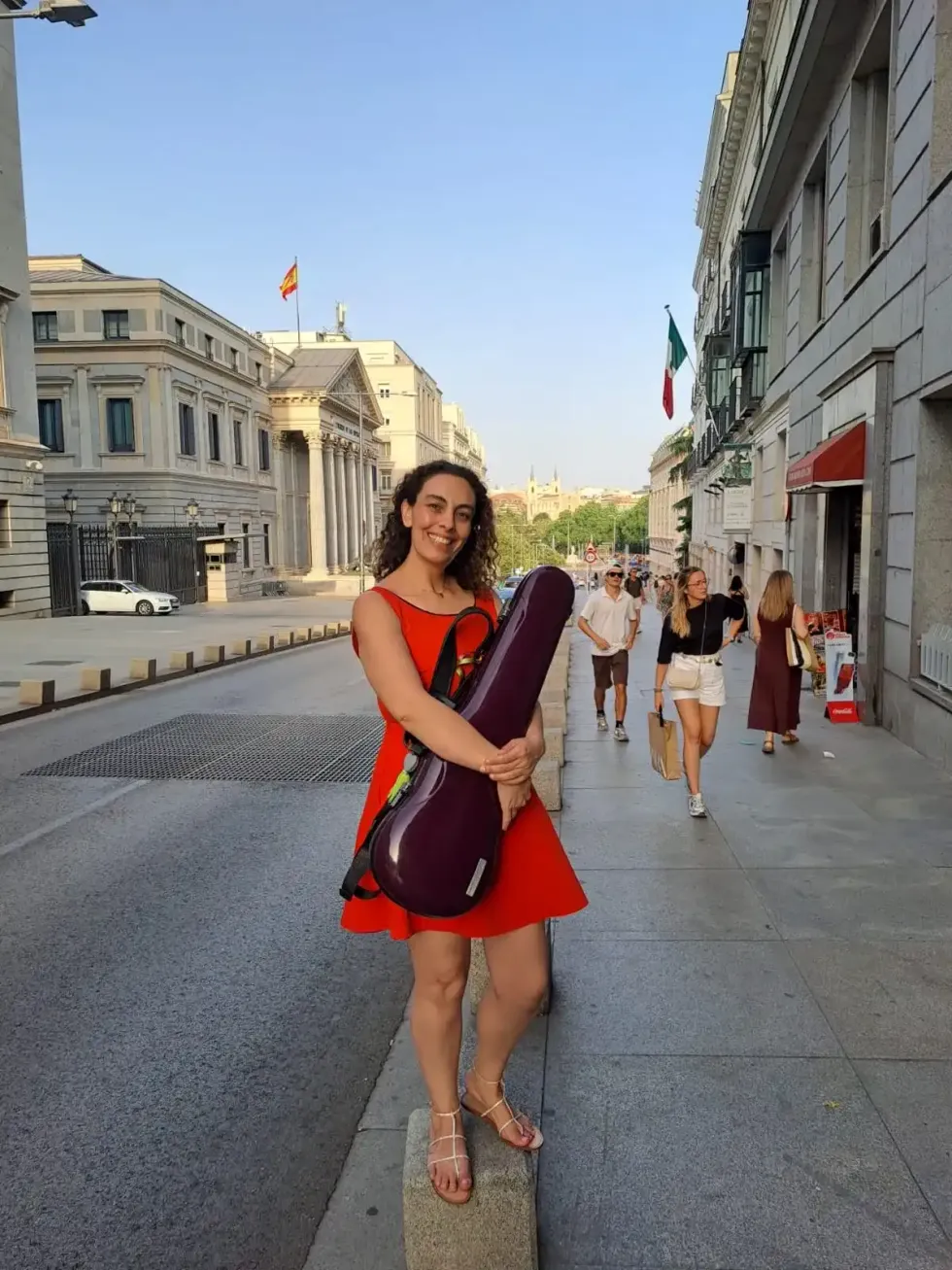 Violinista sostiene su estuche frente al Congreso de los Diputados en Madrid, con bandera de M\u00e9xico al fondo