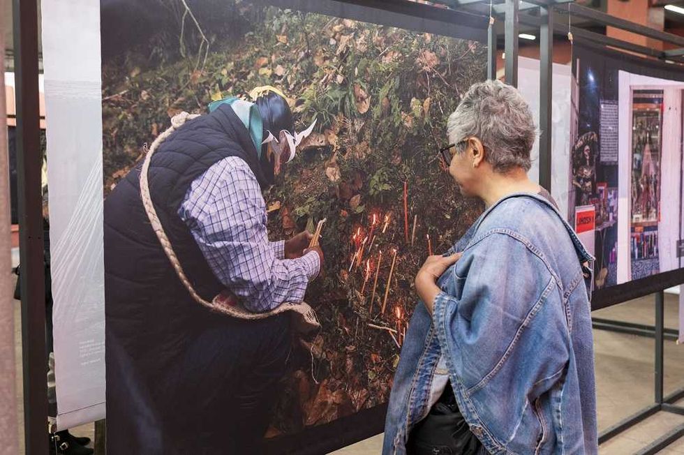 Visitante observa de cerca fotograf\u00eda documental de ritual con velas y hojas en la exposici\u00f3n del concurso nacional de fotograf\u00eda 2026