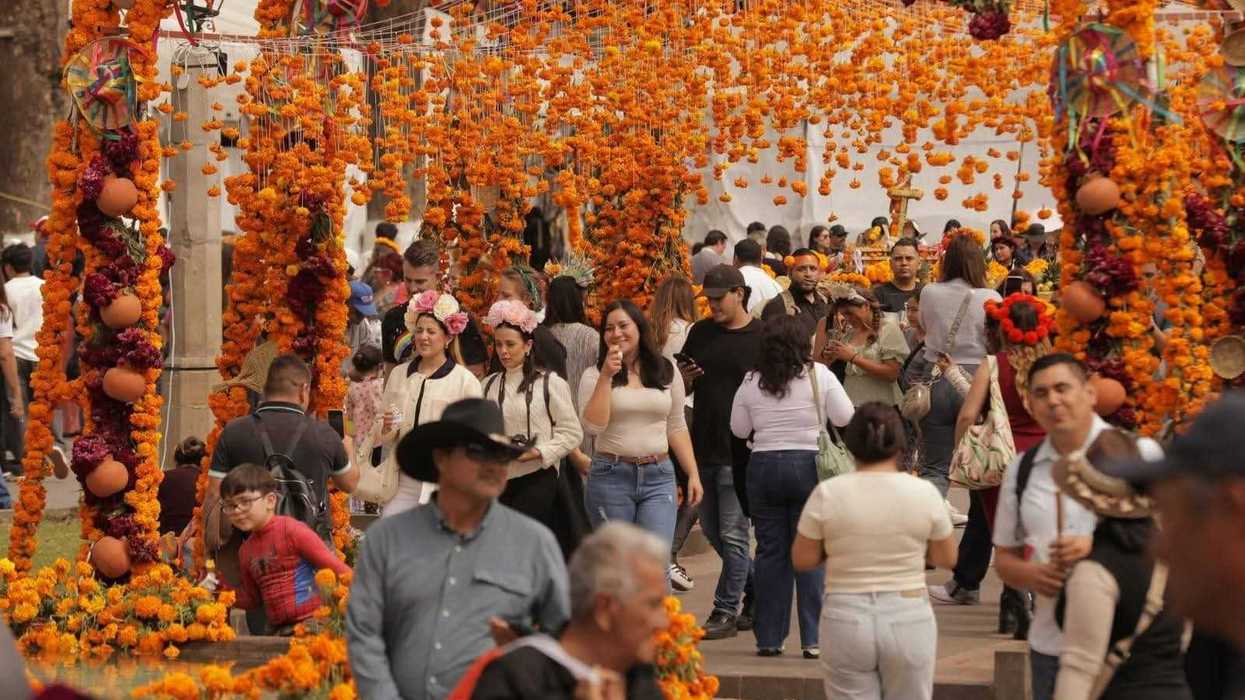 Visitantes entre ofrendas con veladoras y flores de cempasúchil, de noche, en la Noche de Ánimas de Pátzcuaro