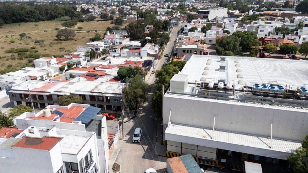 Vista a\u00e9rea de una calle de la colonia Arboledas entre edificios, con un edificio de paneles solares a la izquierda.